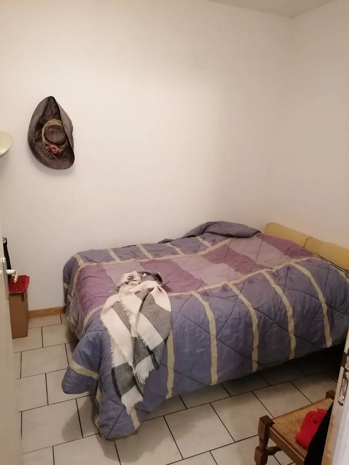 Chambre avec lit double et couvre-lit, chapeau accroché au mur.