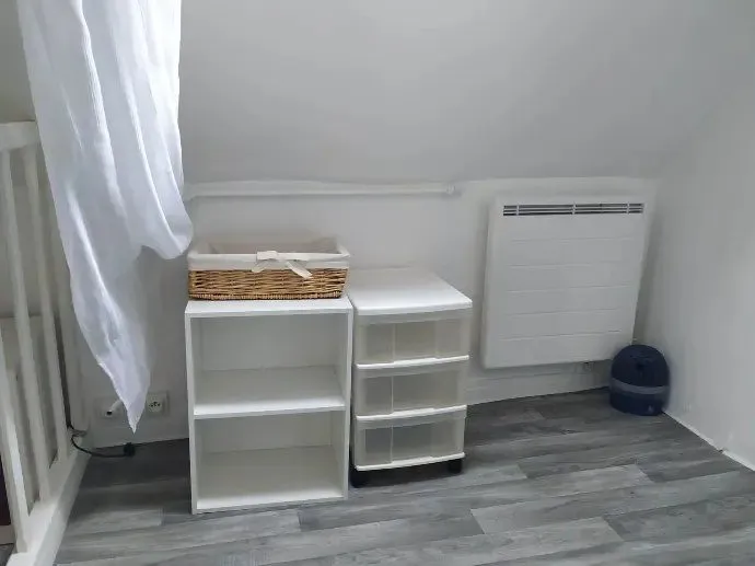 Mezzanine avec bureau blanc, radiateur et rideau.