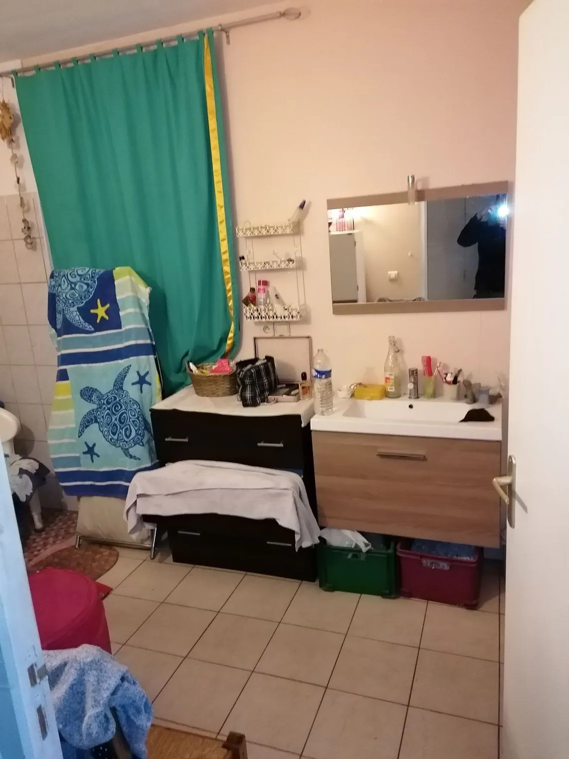 Salle de bains occupée : lavabo, meuble de rangement et rideau vert.