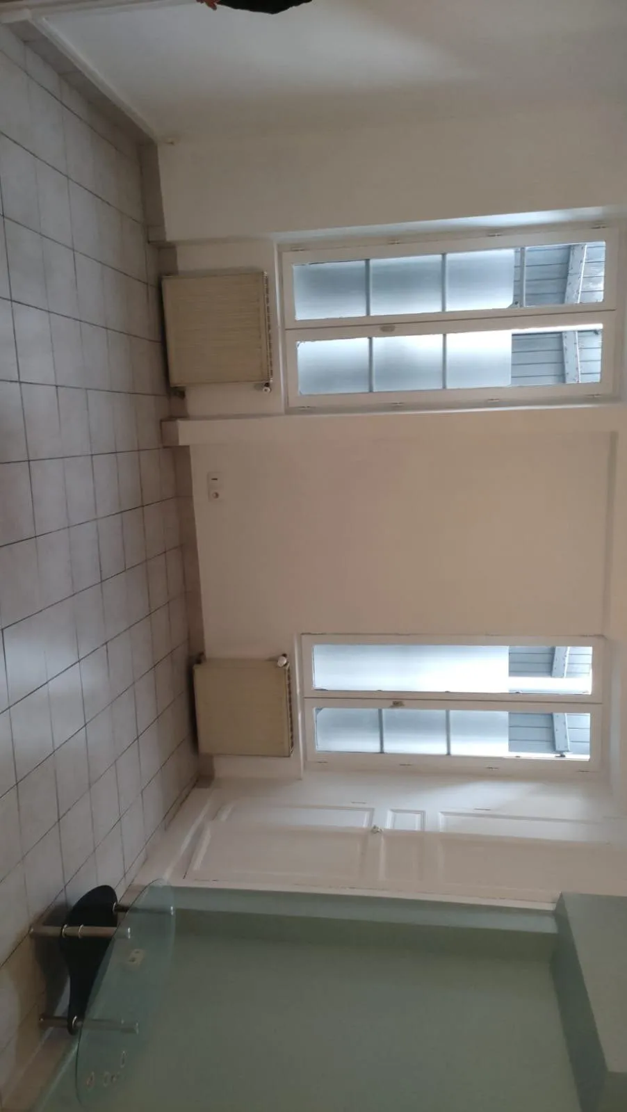 Salle de bains avec baignoire, carrelage clair et deux fenêtres.