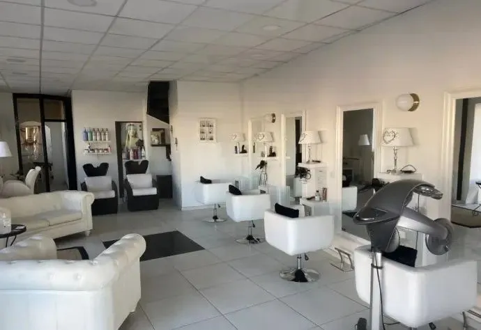 Autre extrémité du salon : postes de coiffage, canapé blanc et sol carrelé.