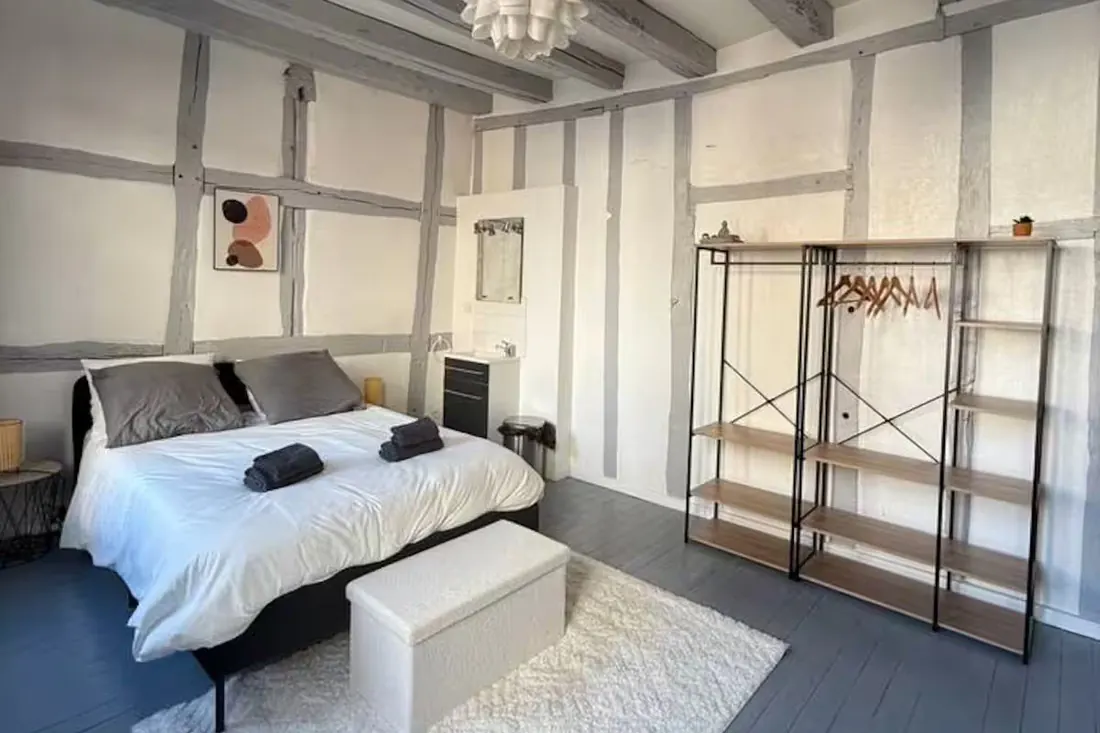 Chambre à colombages rénovée et meublée, lit fait, penderie et étagères posées, prête pour la mise en location.