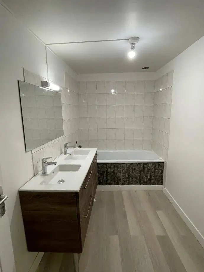 Salle de bains neuve : baignoire, meuble vasque bois et grand miroir.