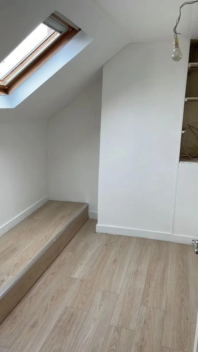 Comble au parquet clair, fenêtre de toit et murs blancs.