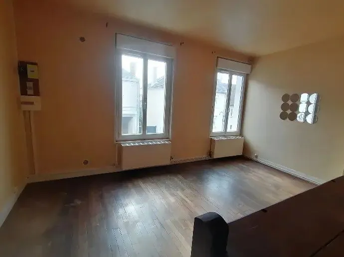 Séjour vide au parquet ancien, deux fenêtres et murs clairs.