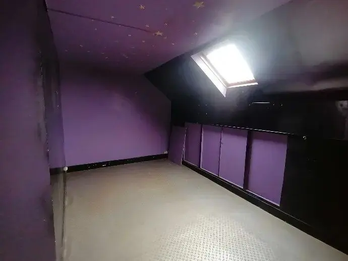 Comble aménagé aux murs violets, sol sombre et fenêtre de toit.