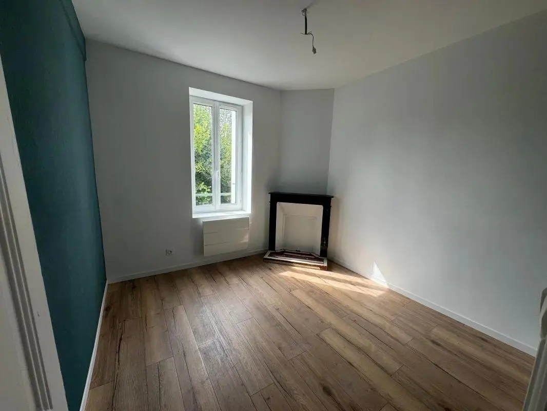 Salon au parquet clair avec mur bleu canard et cheminée conservée.