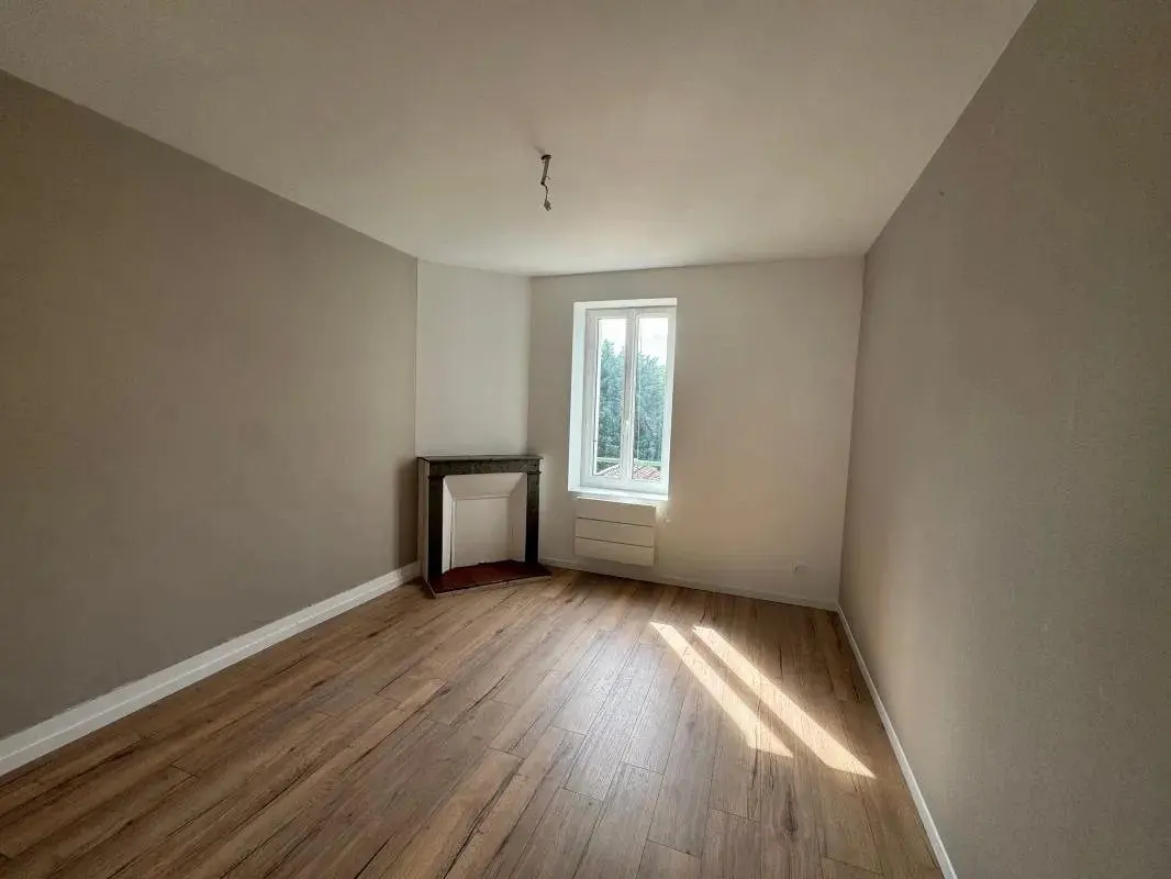 Chambre au parquet clair avec cheminée conservée et fenêtre.