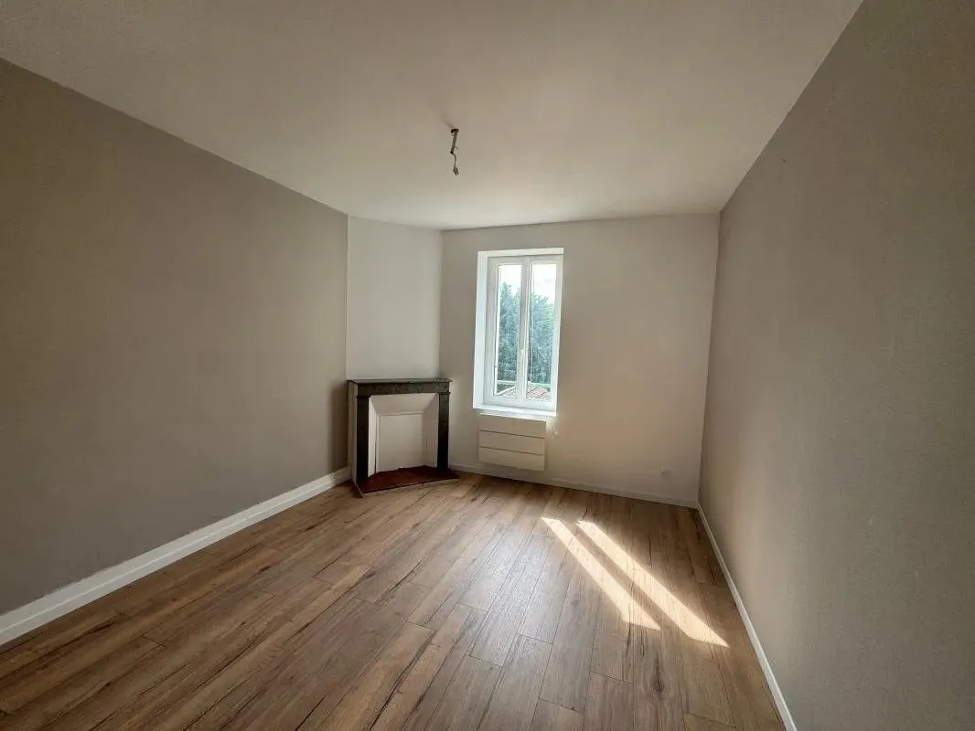 Chambre au parquet clair avec cheminée conservée et fenêtre.