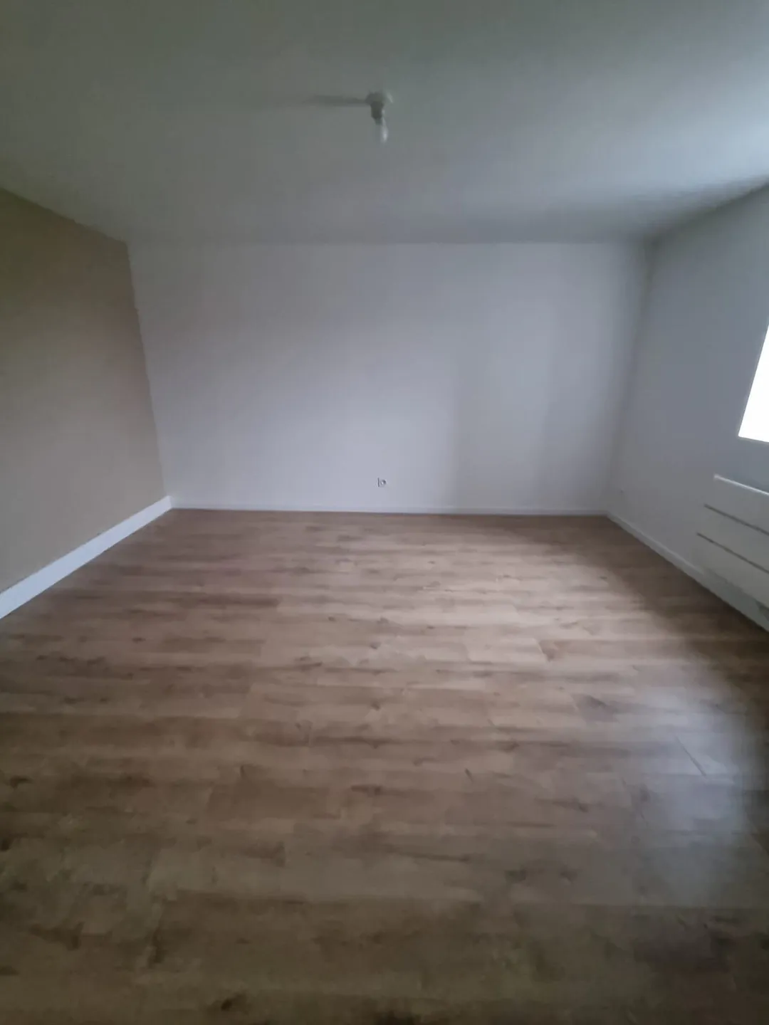 Pièce au parquet clair sous rampant, murs blancs.