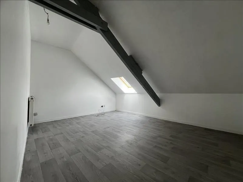Chambre sous rampant repeinte en blanc, poutre apparente et sol gris.