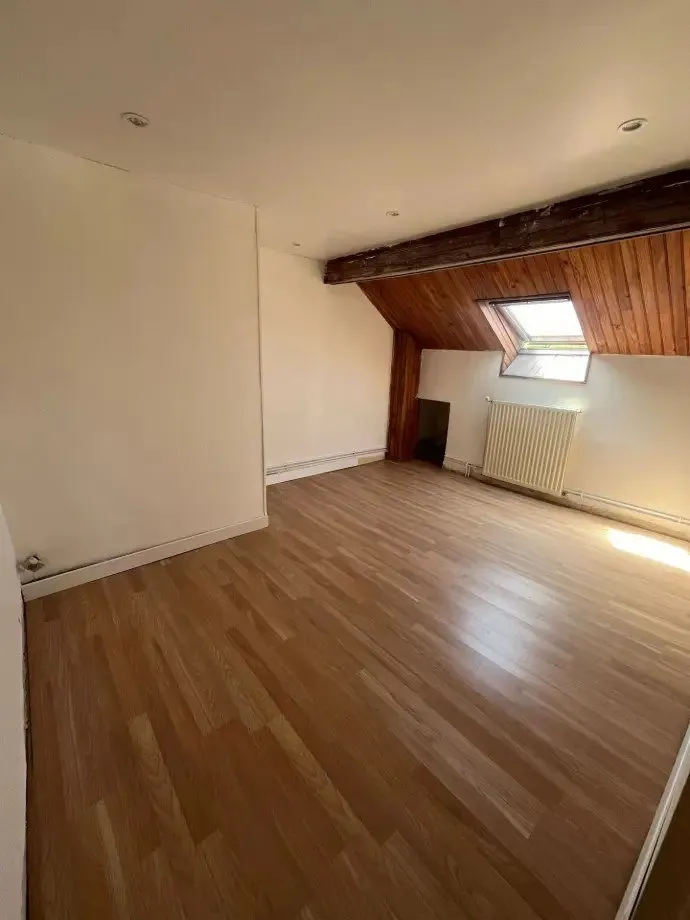Pièce claire sous rampant avec parquet stratifié et fenêtre de toit.