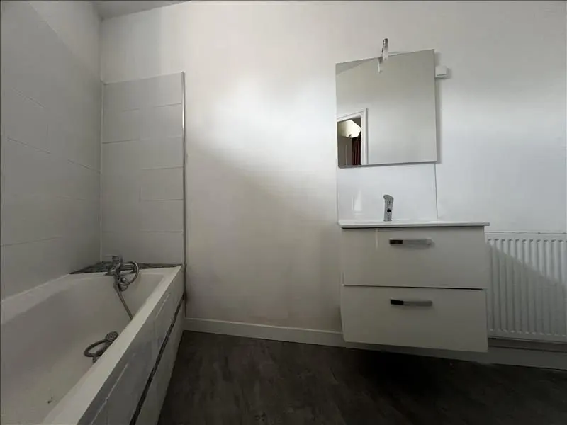 Salle de bains neuve : baignoire, meuble vasque blanc et miroir.