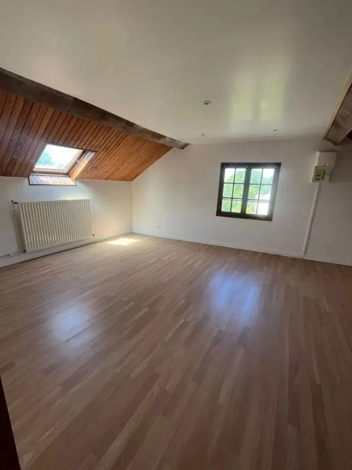 Chambre au parquet clair, plafond lambrissé conservé et fenêtre de toit.