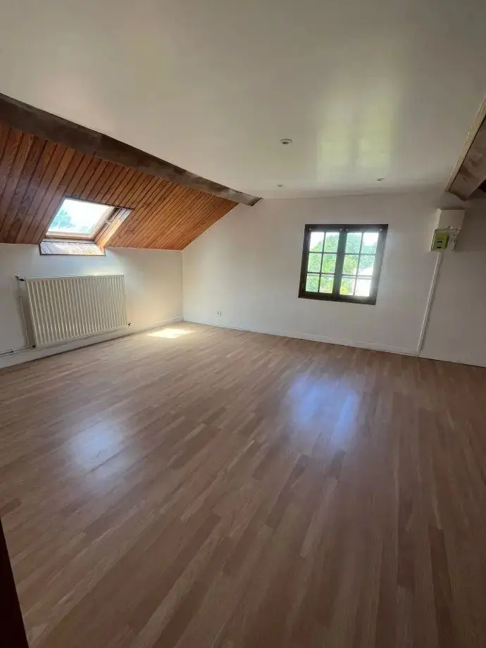 Chambre au parquet clair, plafond lambrissé conservé et fenêtre de toit.