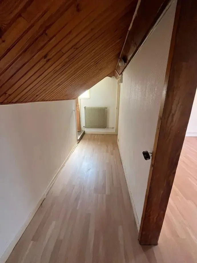 Couloir clair au parquet stratifié, plafond lambrissé.
