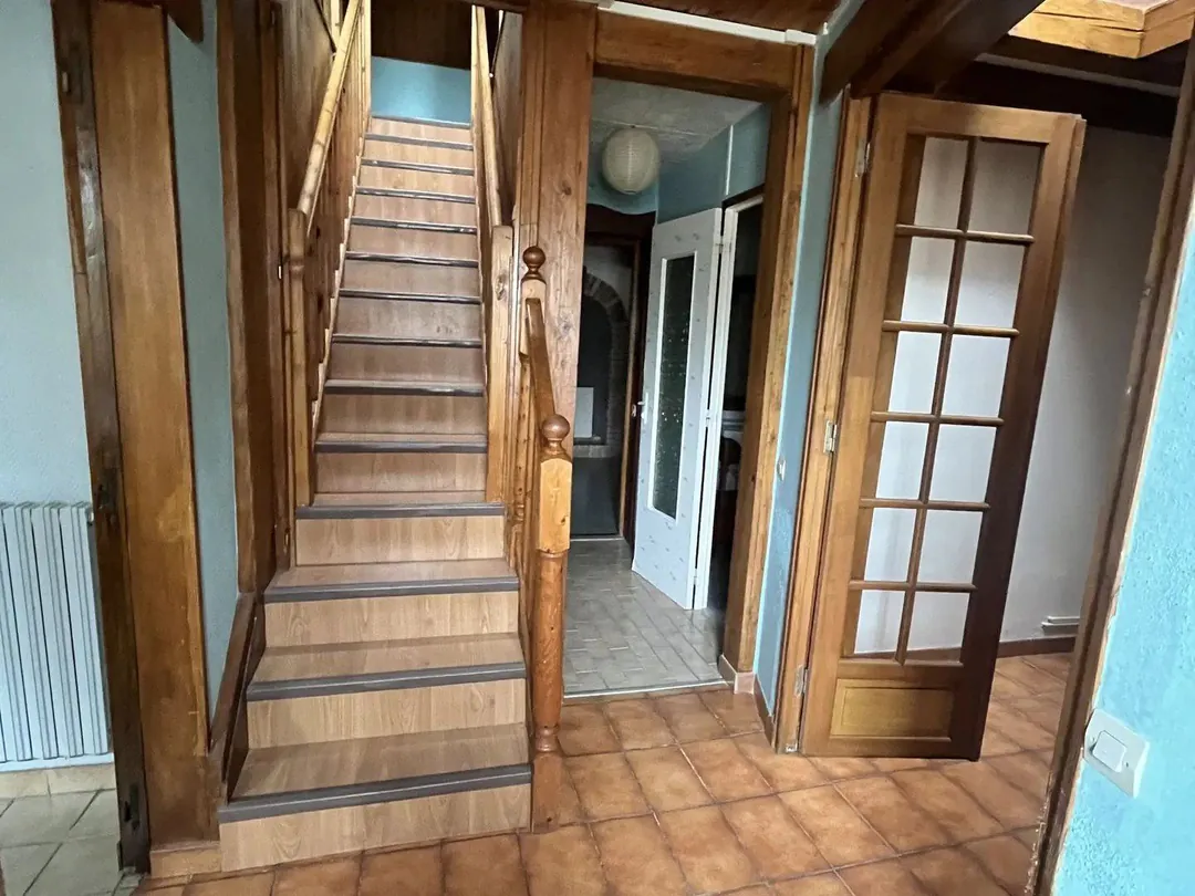 Entrée avec escalier en bois, portes vitrées et sol en tomettes.
