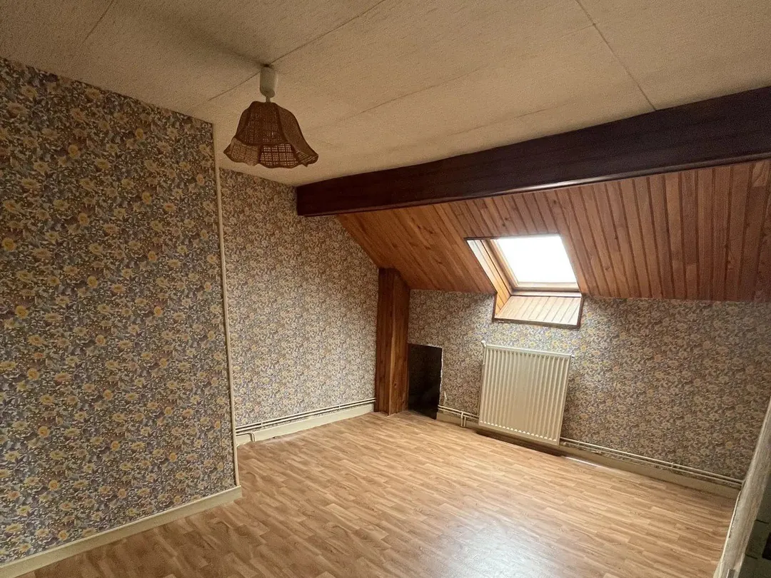 Chambre avec papier peint à motifs, plafond lambrissé et fenêtre de toit.