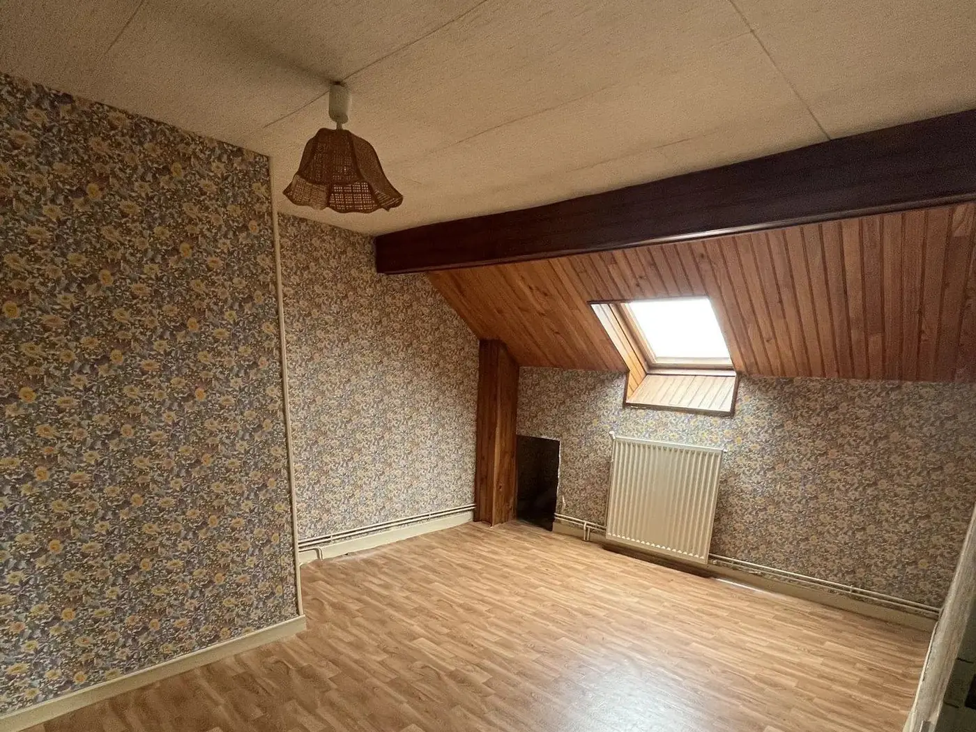 Chambre avec papier peint à motifs, plafond lambrissé et fenêtre de toit.
