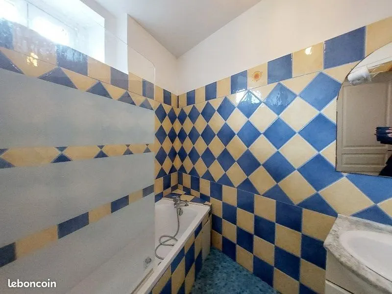 Salle de bains carrelée en damier bleu et jaune, baignoire et lavabo.
