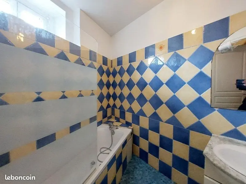 Salle de bains carrelée en damier bleu et jaune, baignoire et lavabo.