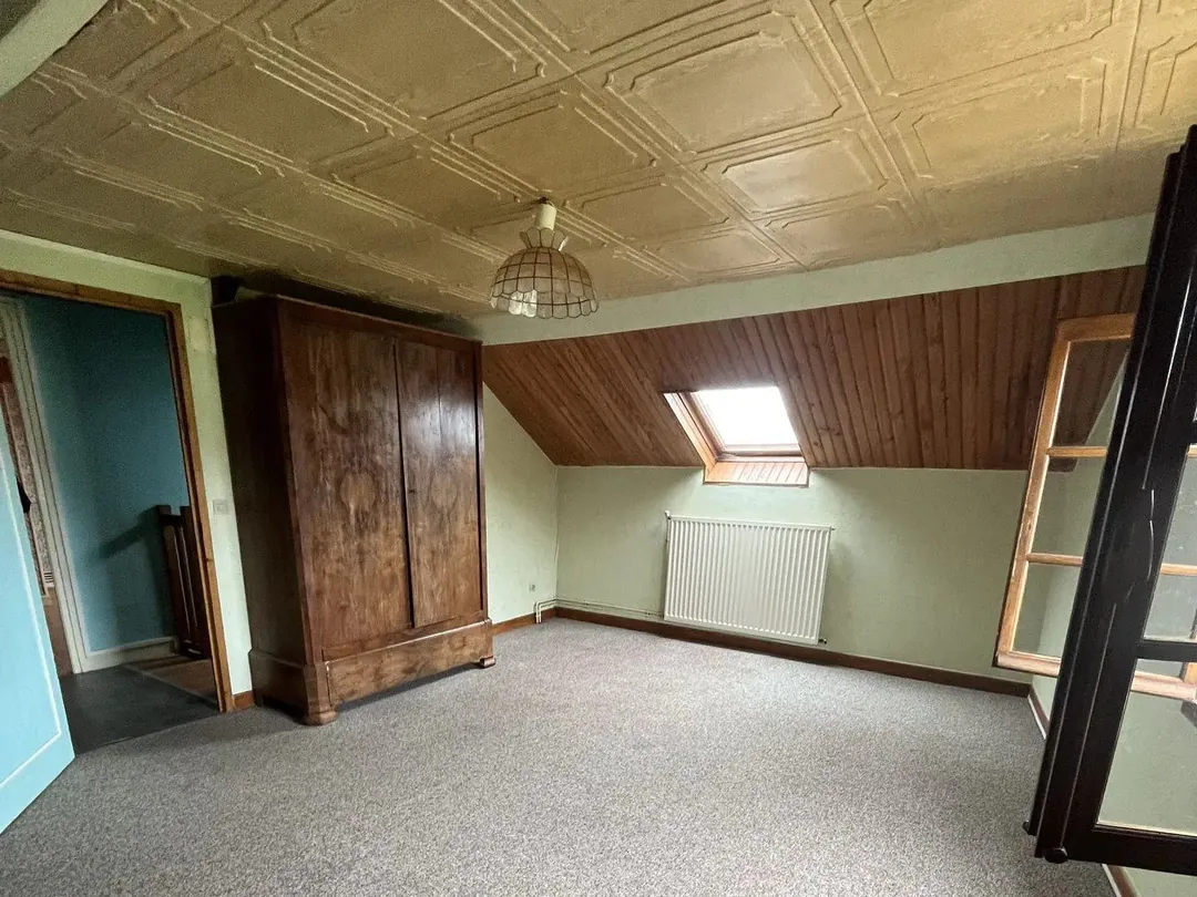 Pièce vide au plafond lambrissé, armoire ancienne et fenêtre de toit.