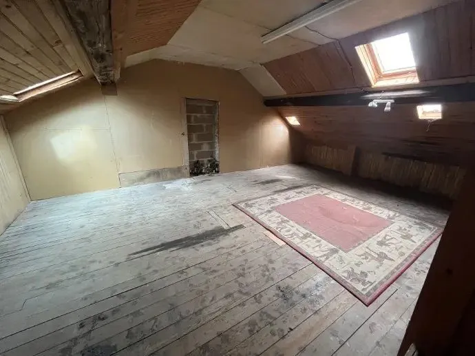 Comble sous charpente apparente avec plancher ancien et tapis.