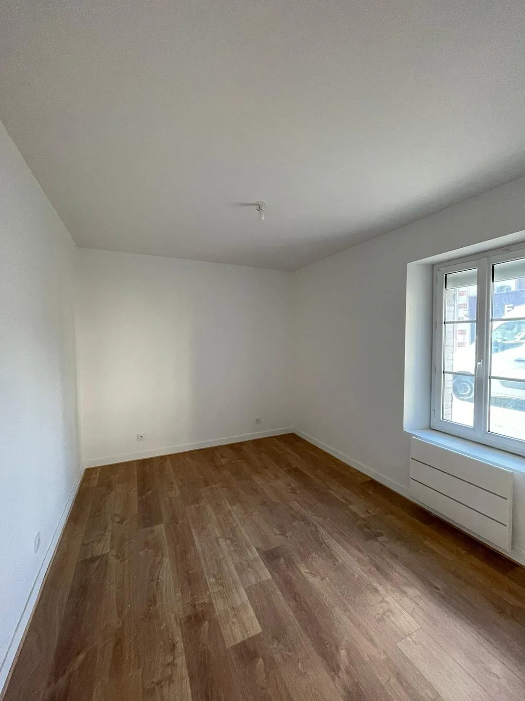Chambre refaite, murs blancs et sol stratifié clair.