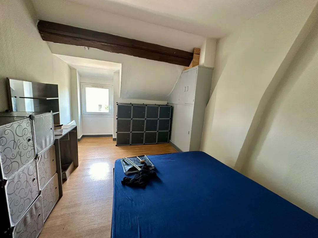 Chambre sous combles avec lit double, commode et poutres apparentes.