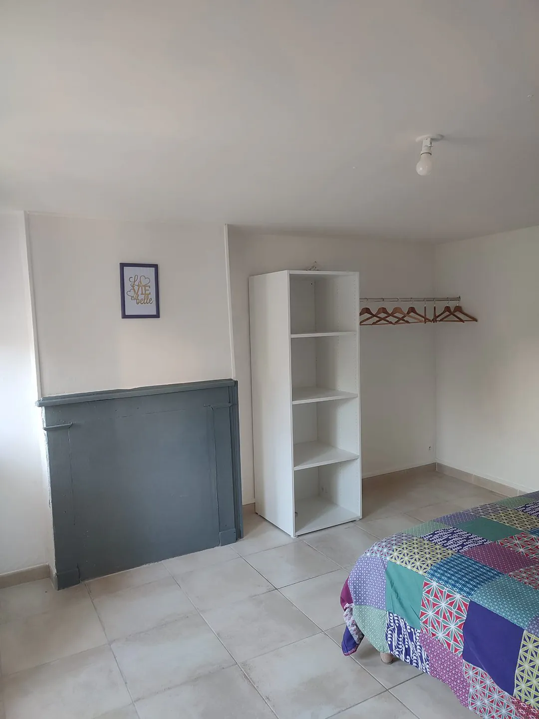 Chambre meublée : lit double, couverture patchwork, étagère et buffet gris.
