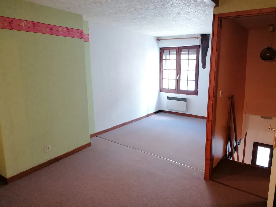 Chambre aux murs verts et frise rose, moquette au sol.