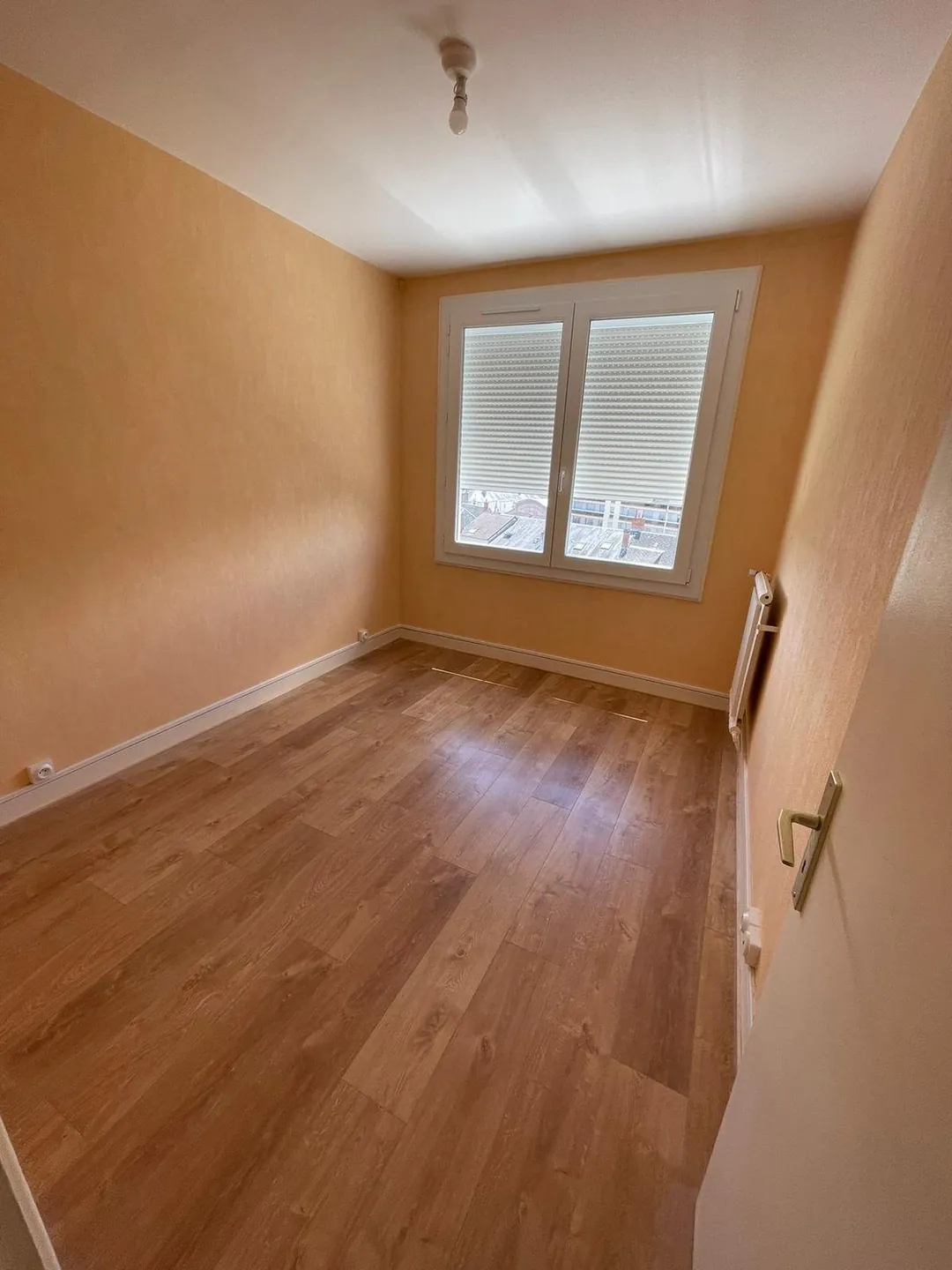 Chambre au parquet clair et mur saumon conservé.