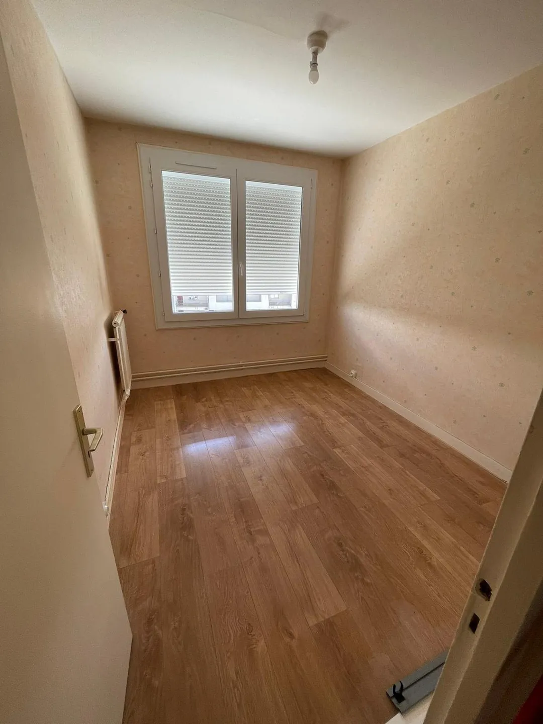 Chambre repeinte, parquet clair et fenêtre à volets.
