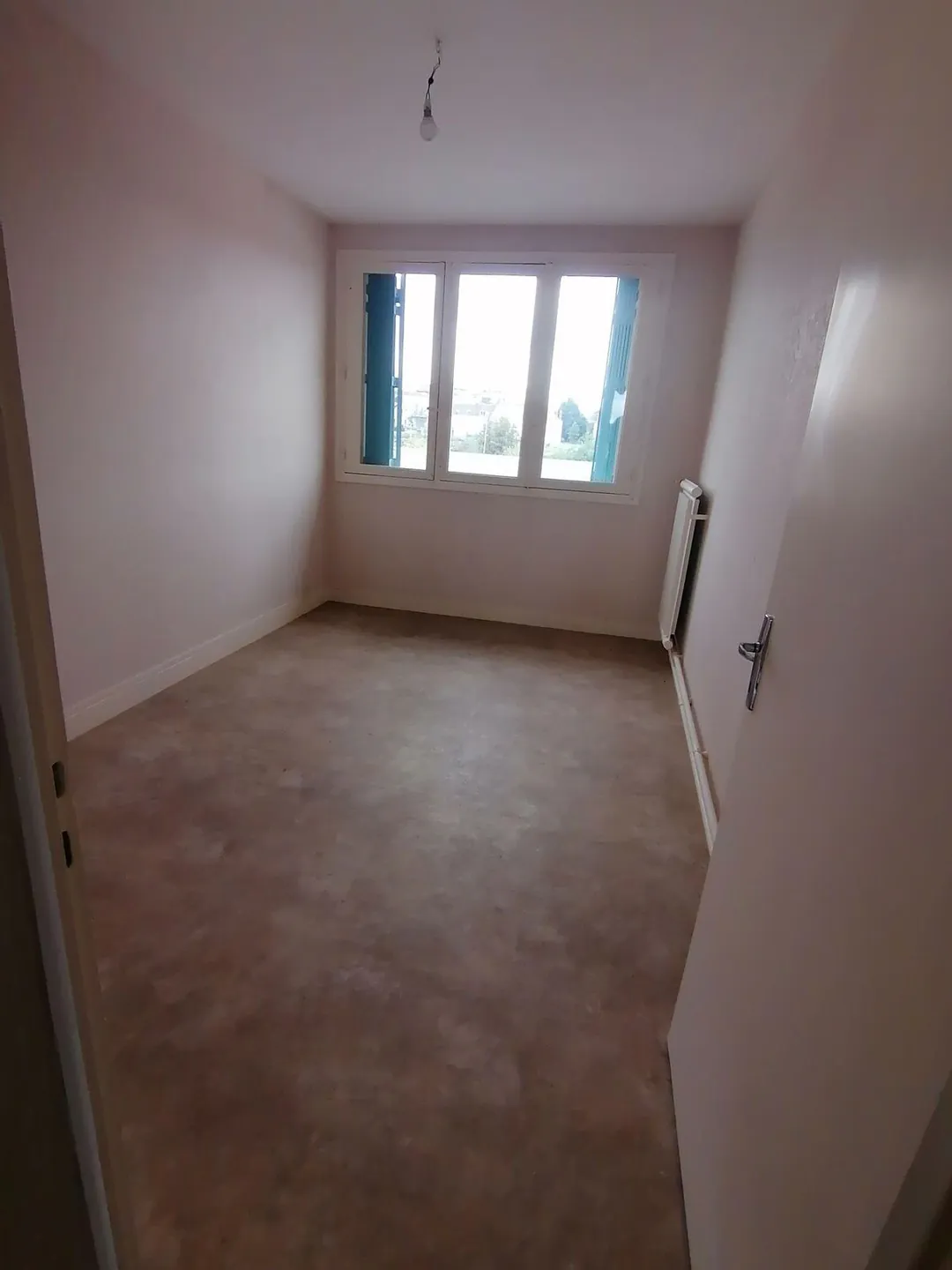 Chambre vide avec moquette usée et murs clairs.