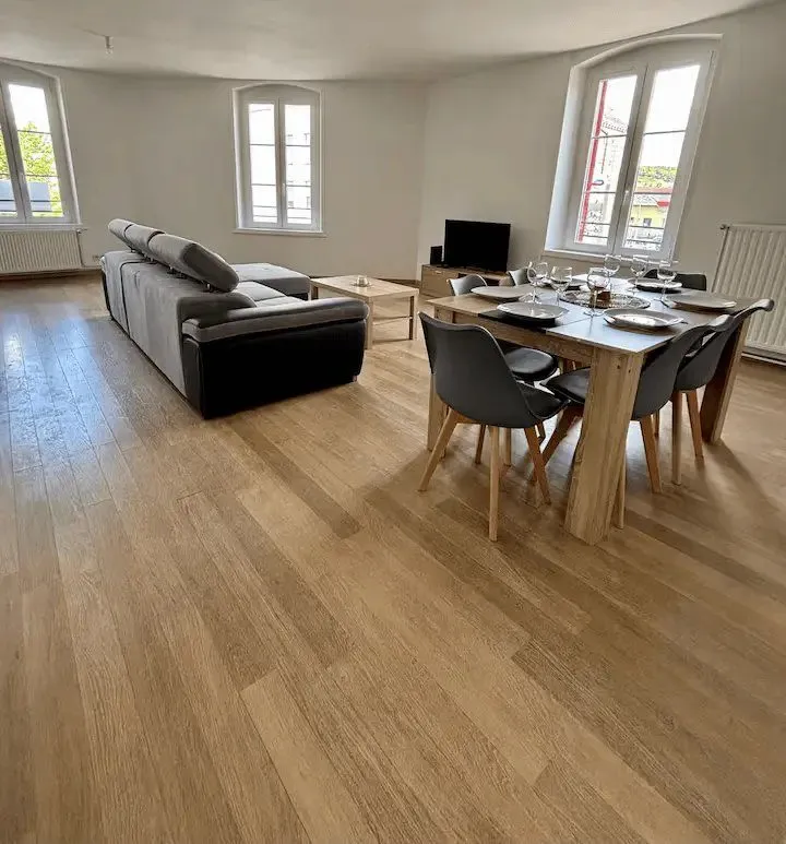 Salle à manger : table et six chaises devant deux fenêtres, parquet clair.