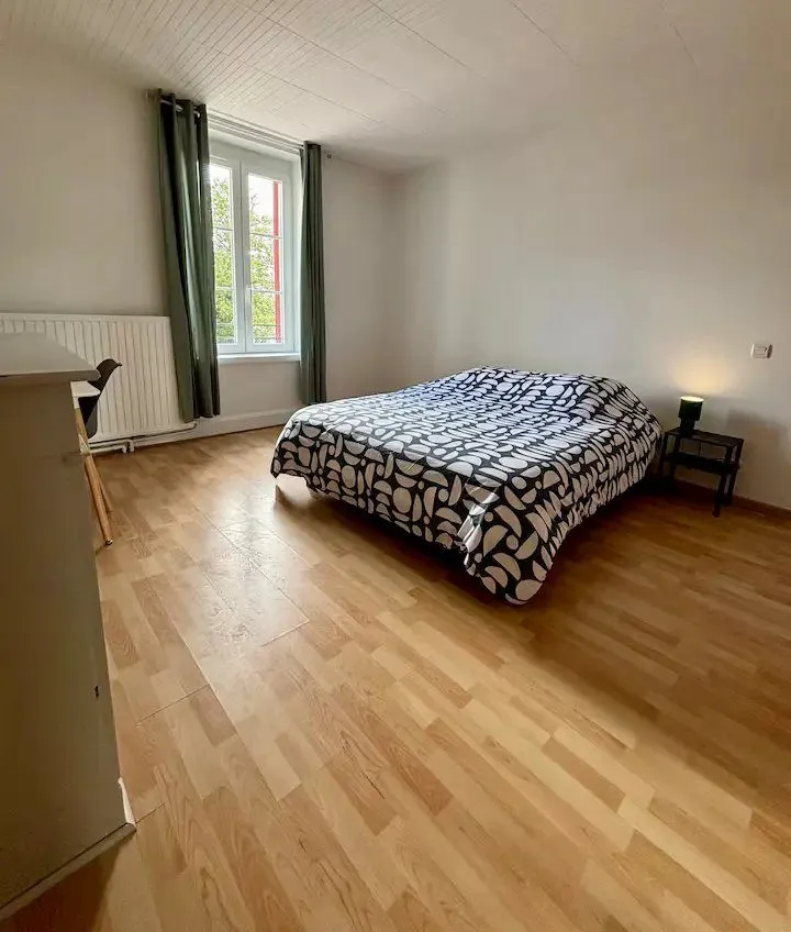 Chambre avec lit double, parquet clair et fenêtre habillée.