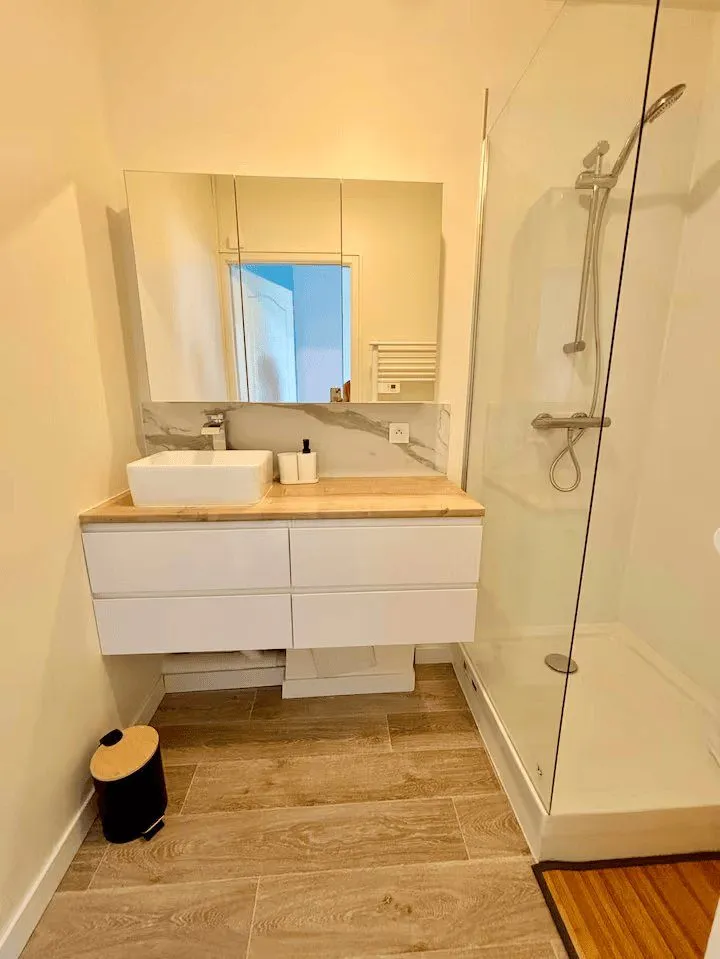 Salle d'eau neuve : douche vitrée, vasque sur meuble blanc et miroir.
