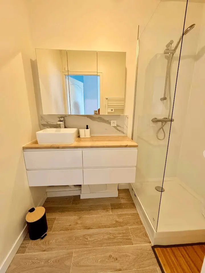 Salle d'eau neuve : douche vitrée, vasque sur meuble blanc et miroir.