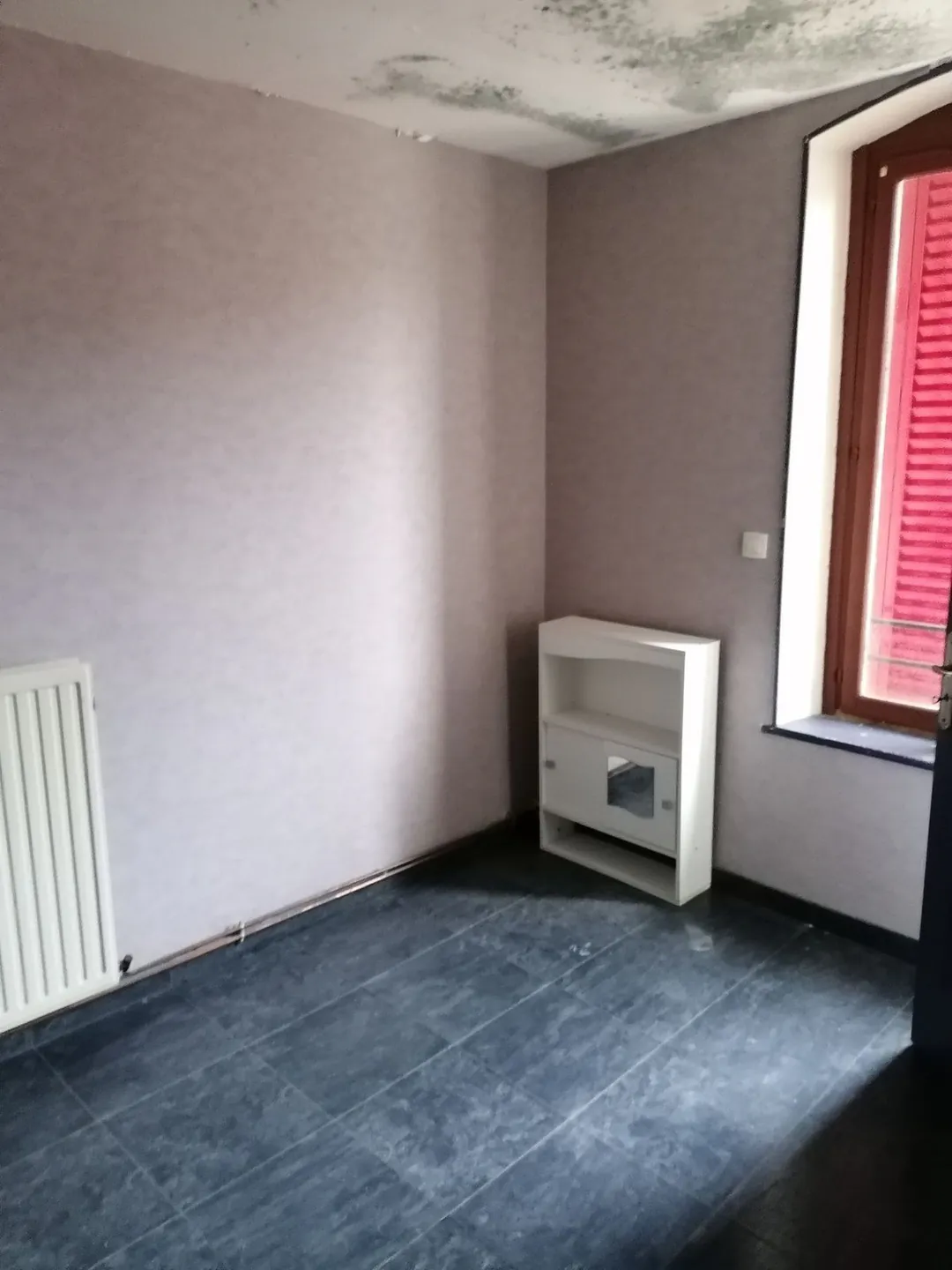 Chambre vide, murs tachés d'humidité près du plafond, sol sombre.