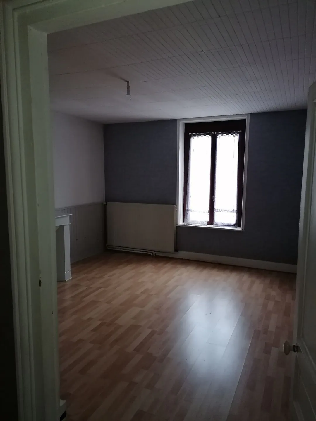 Pièce vide au parquet ancien avec encadrement de porte sombre.