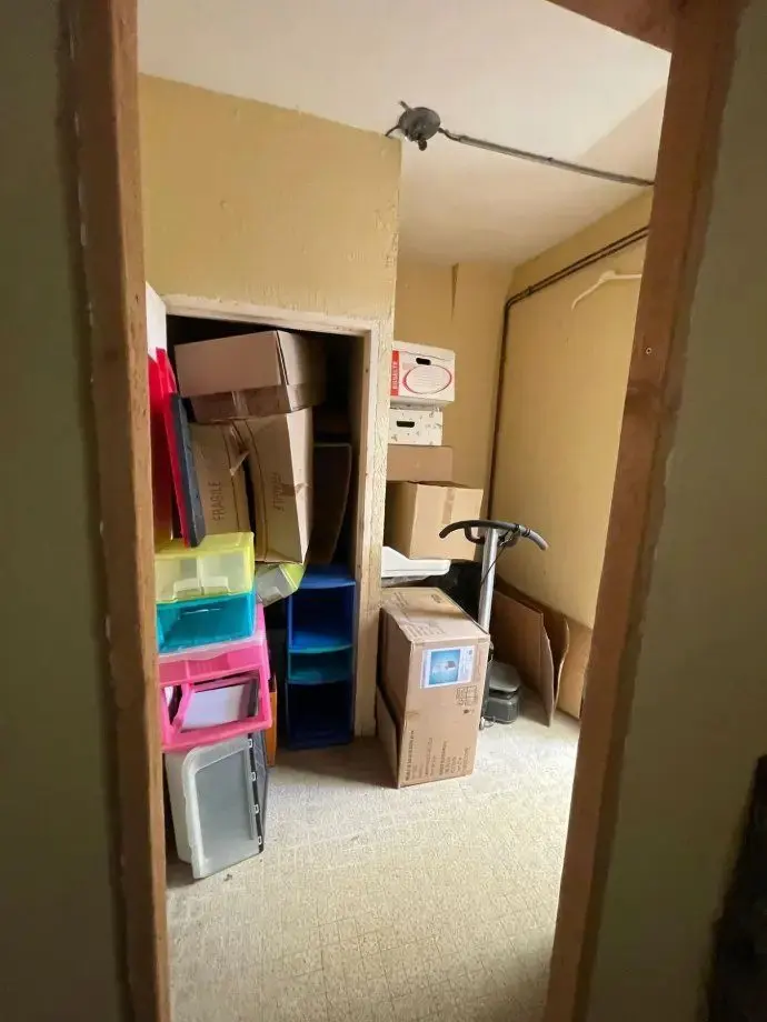 Ancienne réserve encombrée de cartons, de bacs de rangement et de matériel.