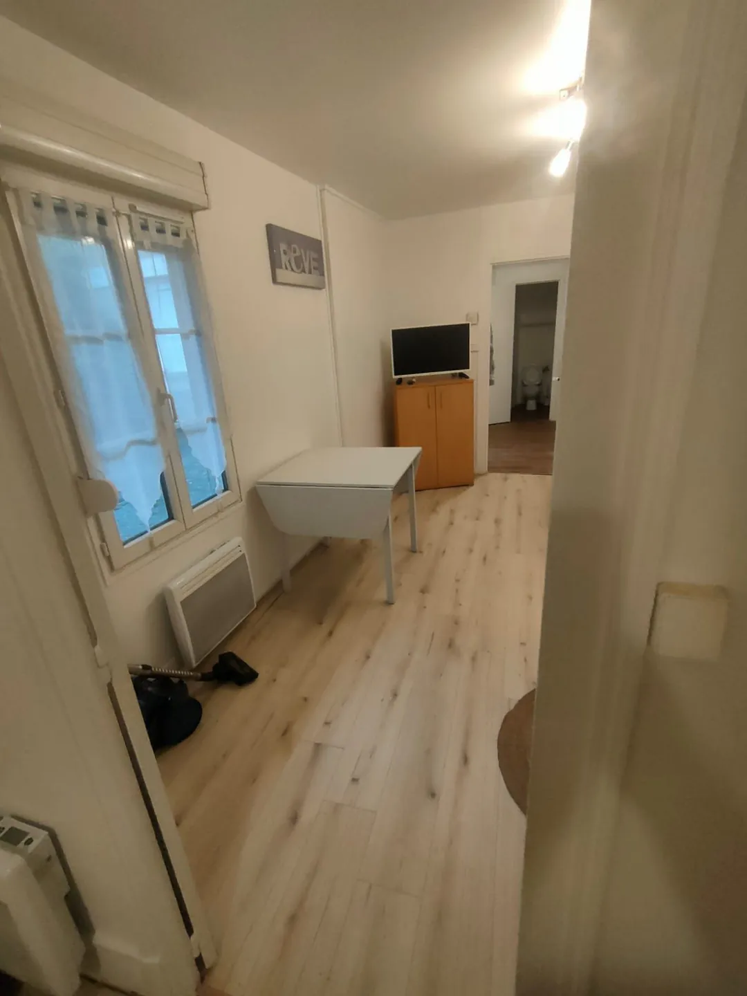 Séjour vu depuis le coin nuit : fenêtre, bureau, téléviseur et rangements.