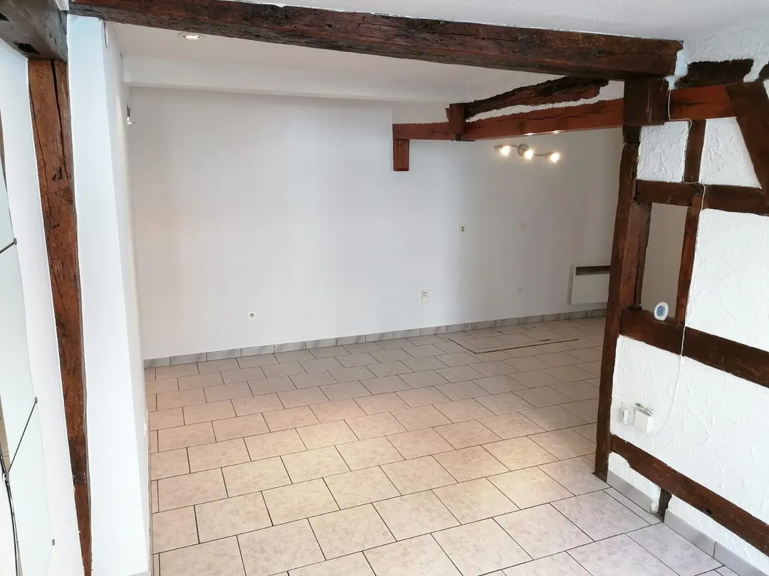 Le séjour vide, poutres et colombages apparents, carrelage clair au sol.