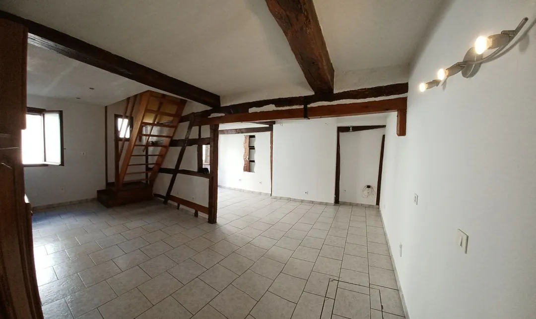 Le séjour vide avec l'escalier au fond et les poutres apparentes.