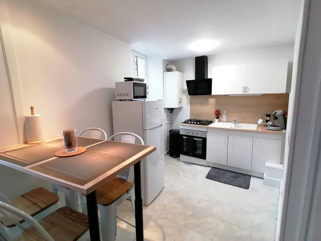 Cuisine équipée blanche avec hotte, four, table haute et tabourets.