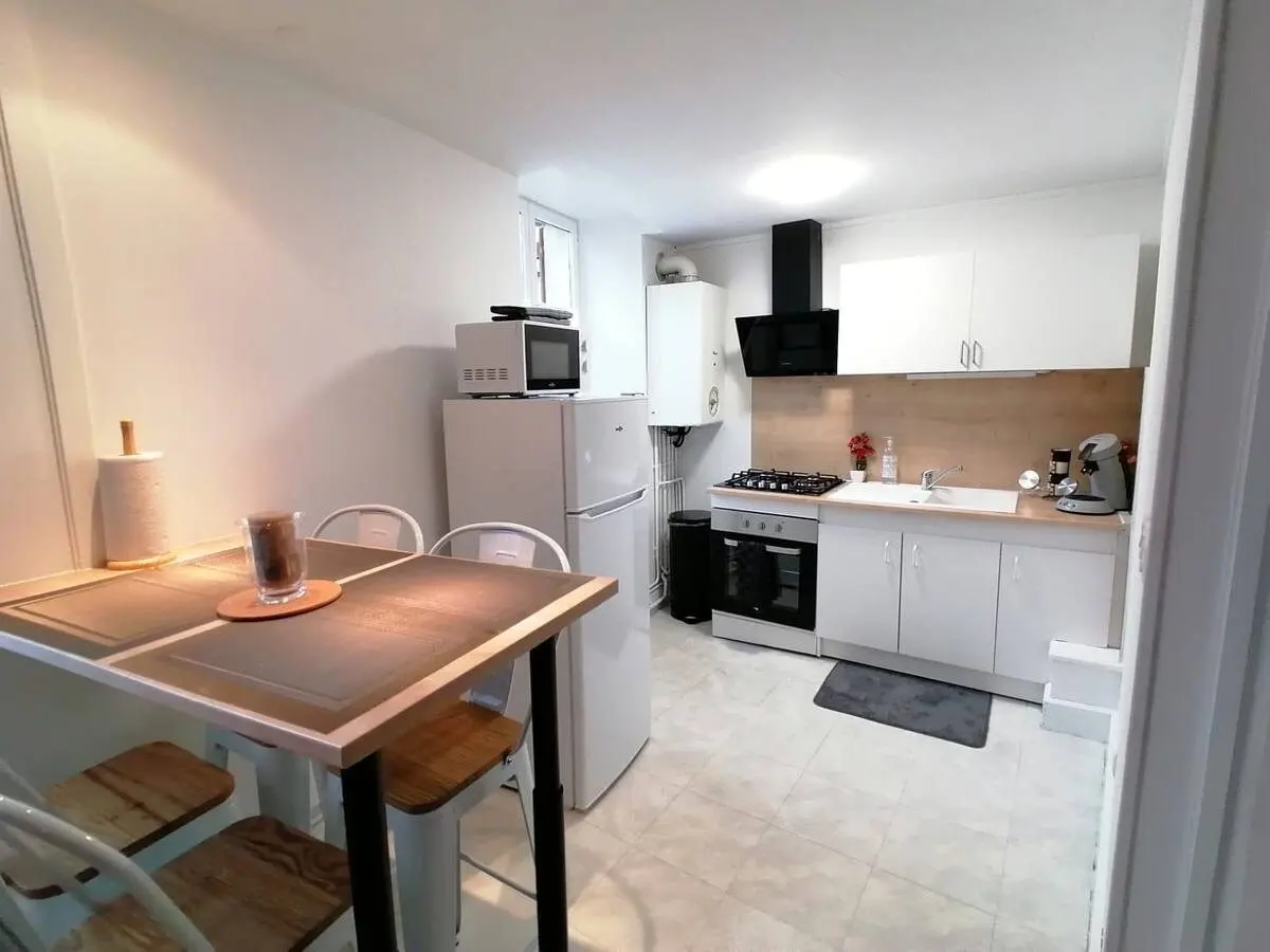 Cuisine équipée blanche avec hotte, four, table haute et tabourets.