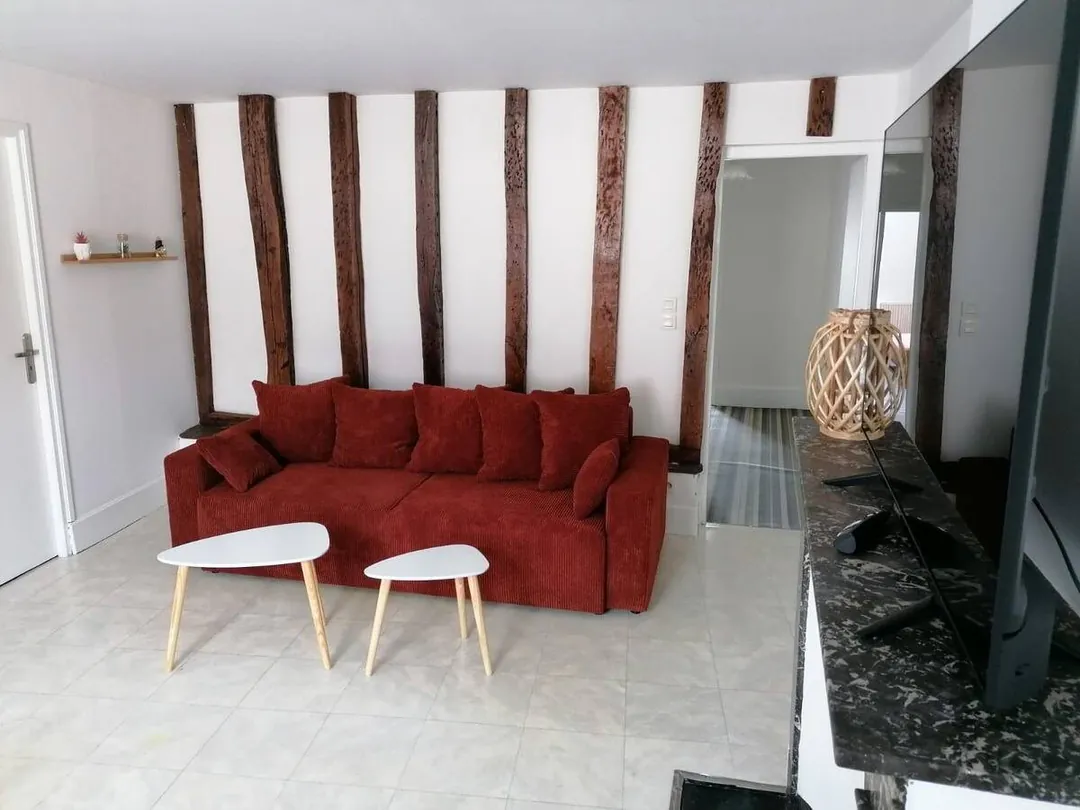 Coin salon sous colombages avec canapé rouge, tables basses et miroir.
