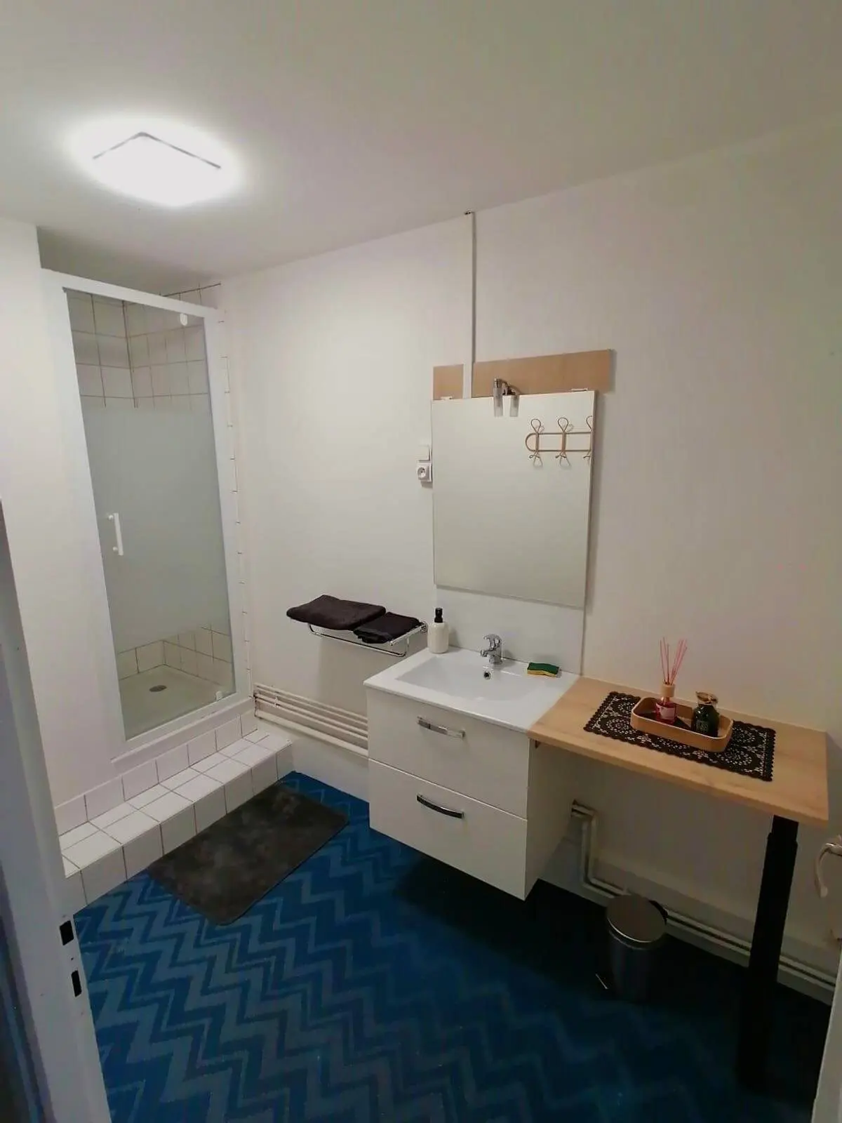 Salle d'eau neuve : douche vitrée, vasque sur plan bois et sol à chevrons.