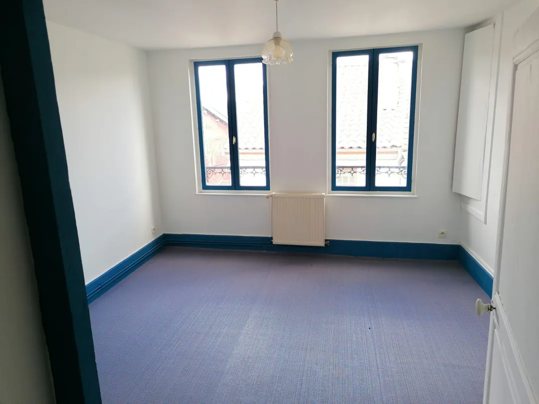 Pièce vide avec deux fenêtres, sol bleu et murs blancs.