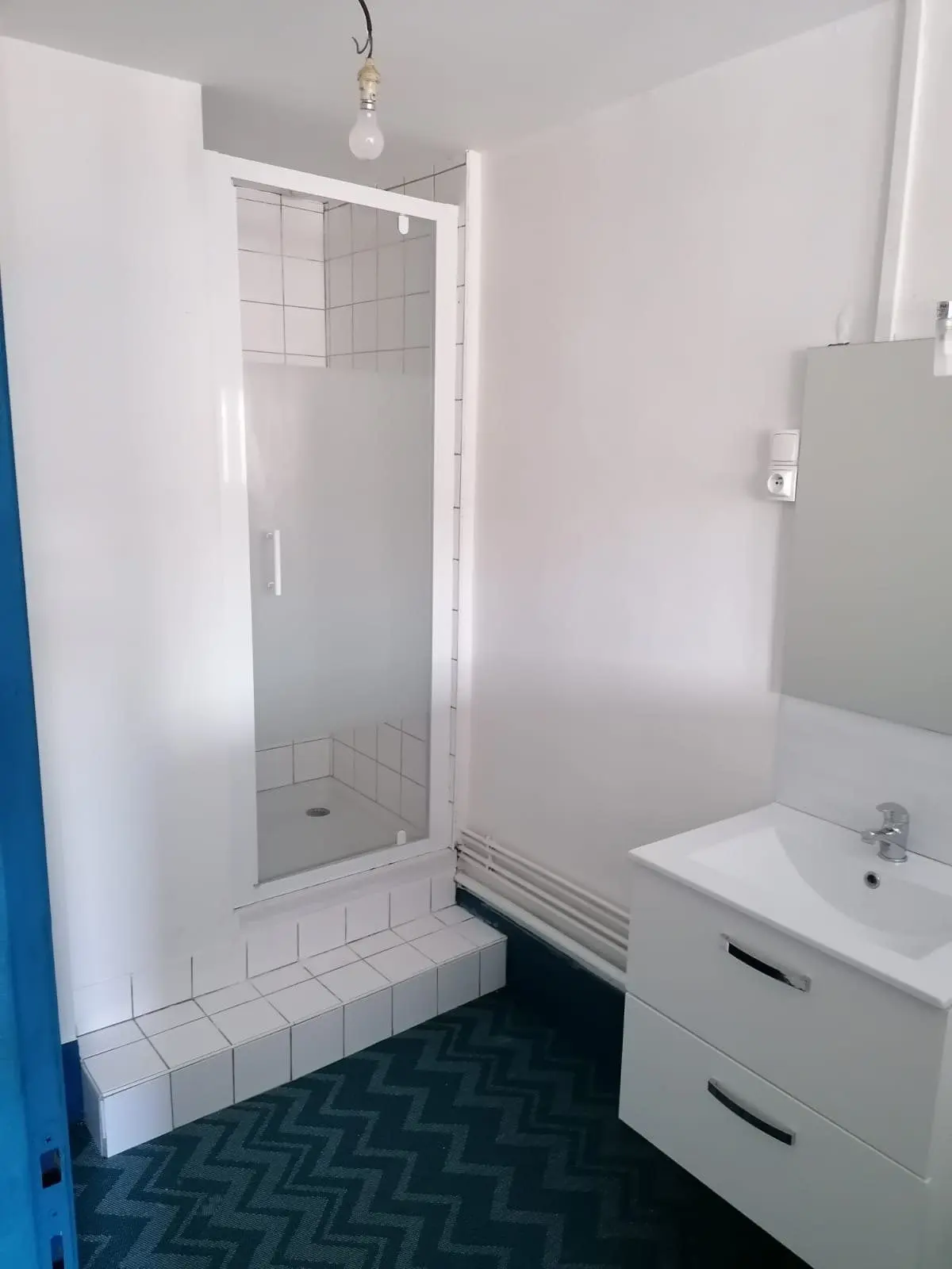 Salle d'eau avec cabine de douche, meuble vasque et sol à chevrons bleus.